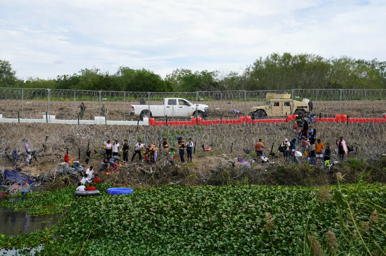 2023年12月29日，從墨西哥馬塔莫羅斯看到，人們?cè)诘驴怂_斯州布朗斯維爾的鐵絲網(wǎng)和新安裝的路障后面等待向美國(guó)邊境當(dāng)局自首。