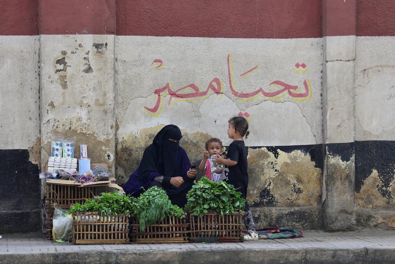 2023年10月10日，埃及開羅，一名帶著孩子的街頭小販坐在一幅壁畫前，壁畫上有埃及國旗和&ldquo;埃及萬歲&rdquo;的文字。